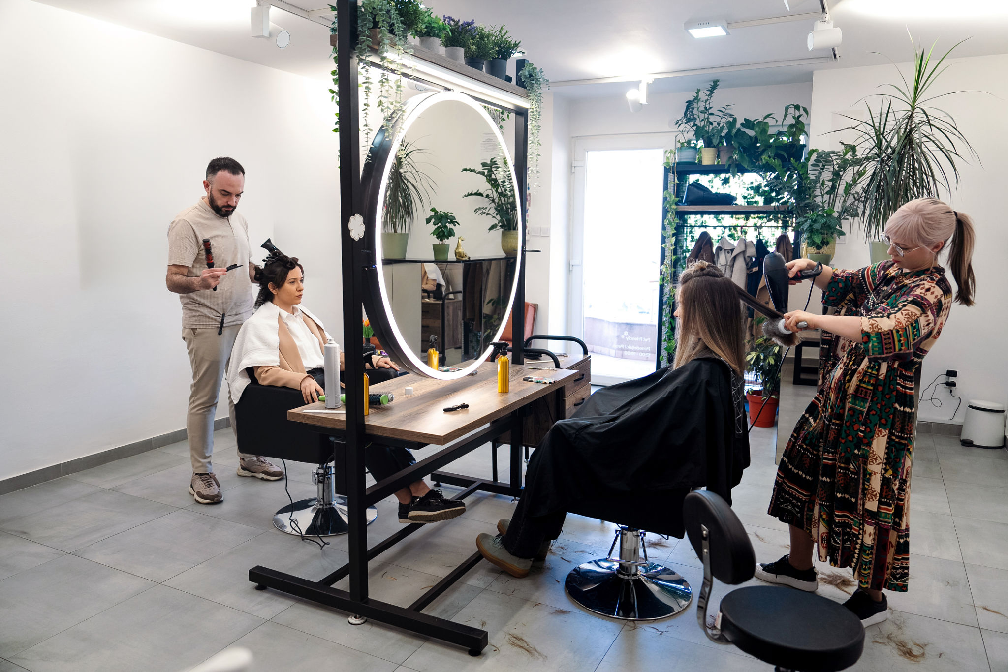Male and a female hairstylist are working on two separate female clients in a stylish, modern hair salon